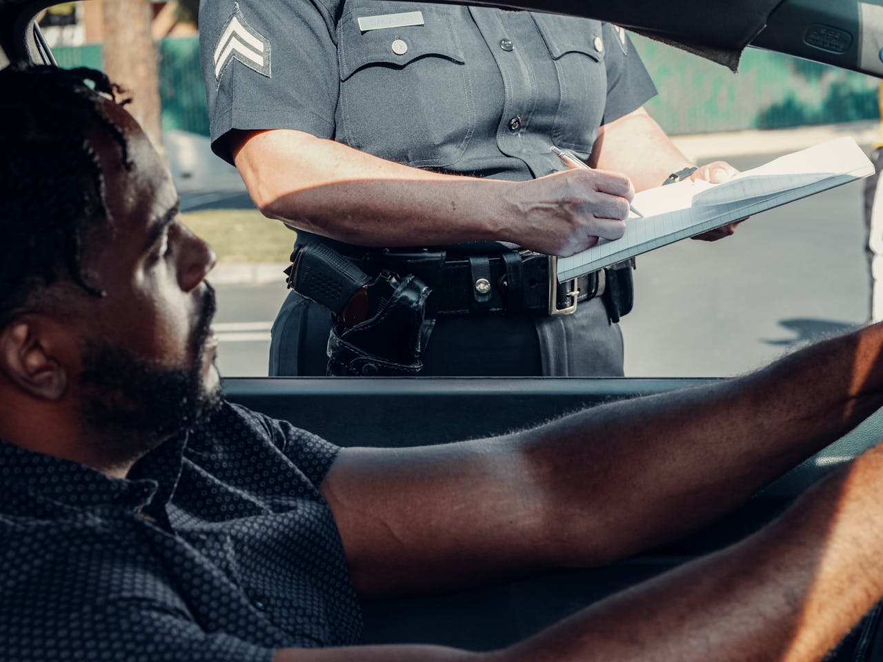 A Man Sitting Inside the Car Looking at the Police Officer Writing on the Traffic Ticket